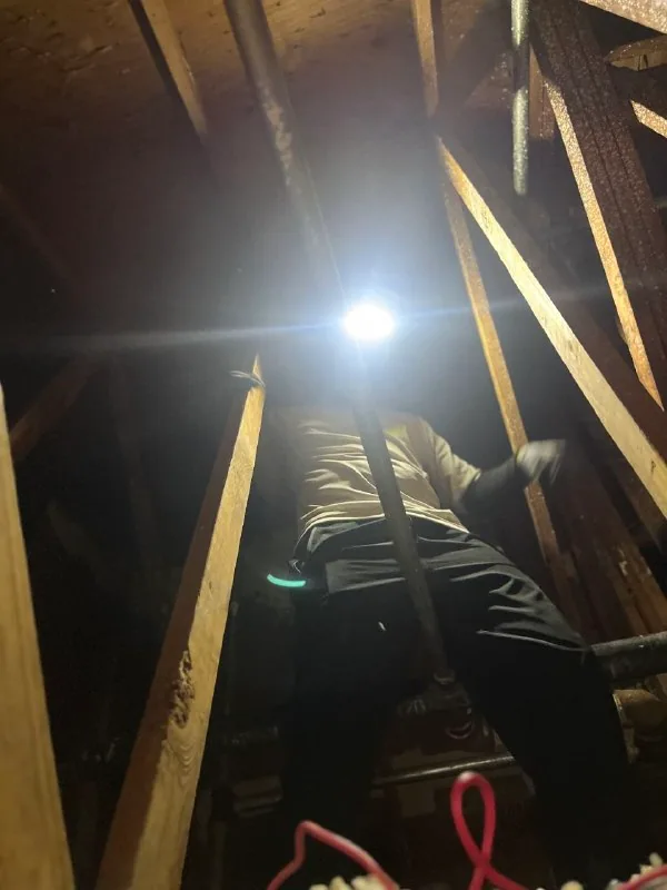 Technician pulling low-voltage cable through an attic framing cavity