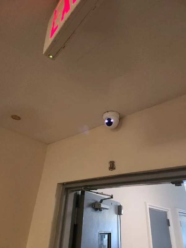 Dome security camera mounted above an interior doorway beneath an exit sign
