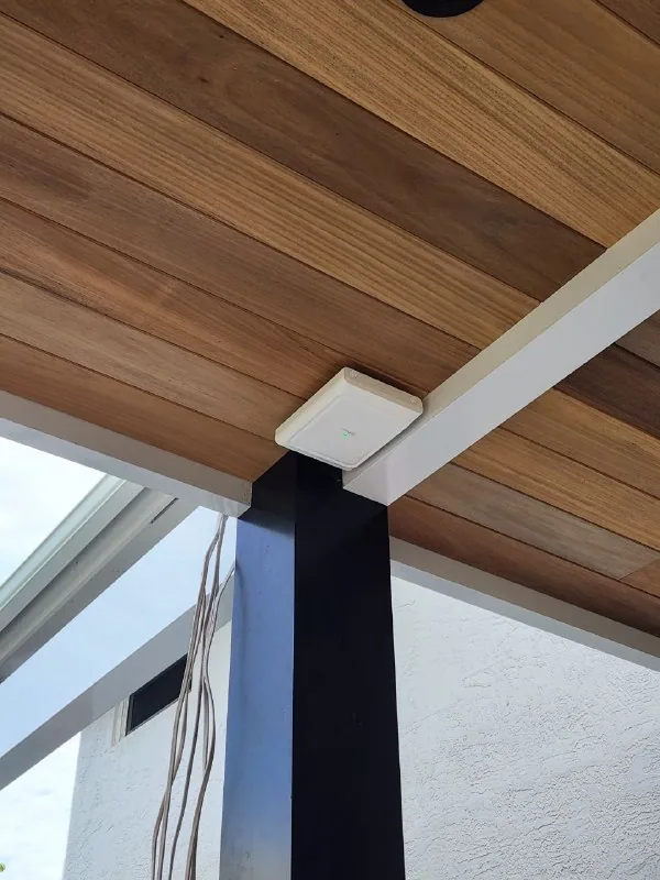 White wireless access point mounted at the corner of a wood pergola ceiling