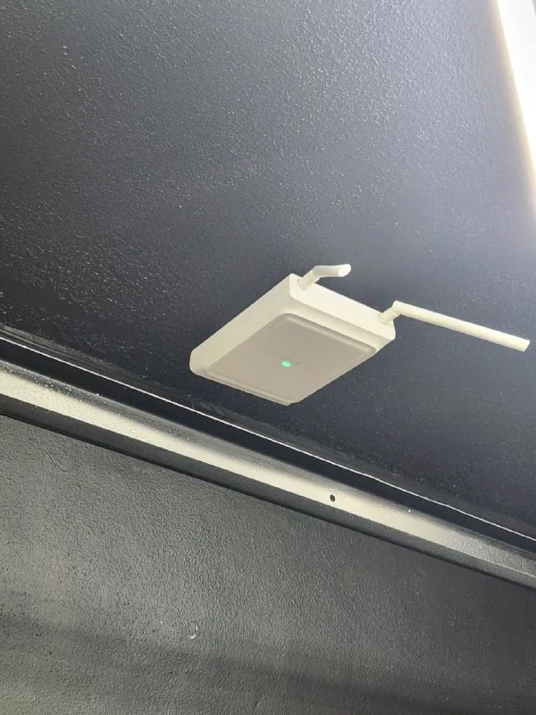 White wireless access point with external antennas mounted to a dark ceiling