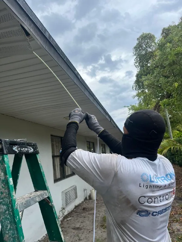 Technician routing exterior low-voltage cable beneath a building soffit from a ladder